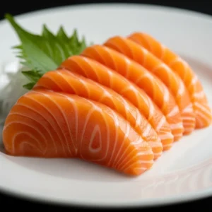 Close up de seis fatias de sashimi de salmão em prato branco. Folha verde ao fundo.